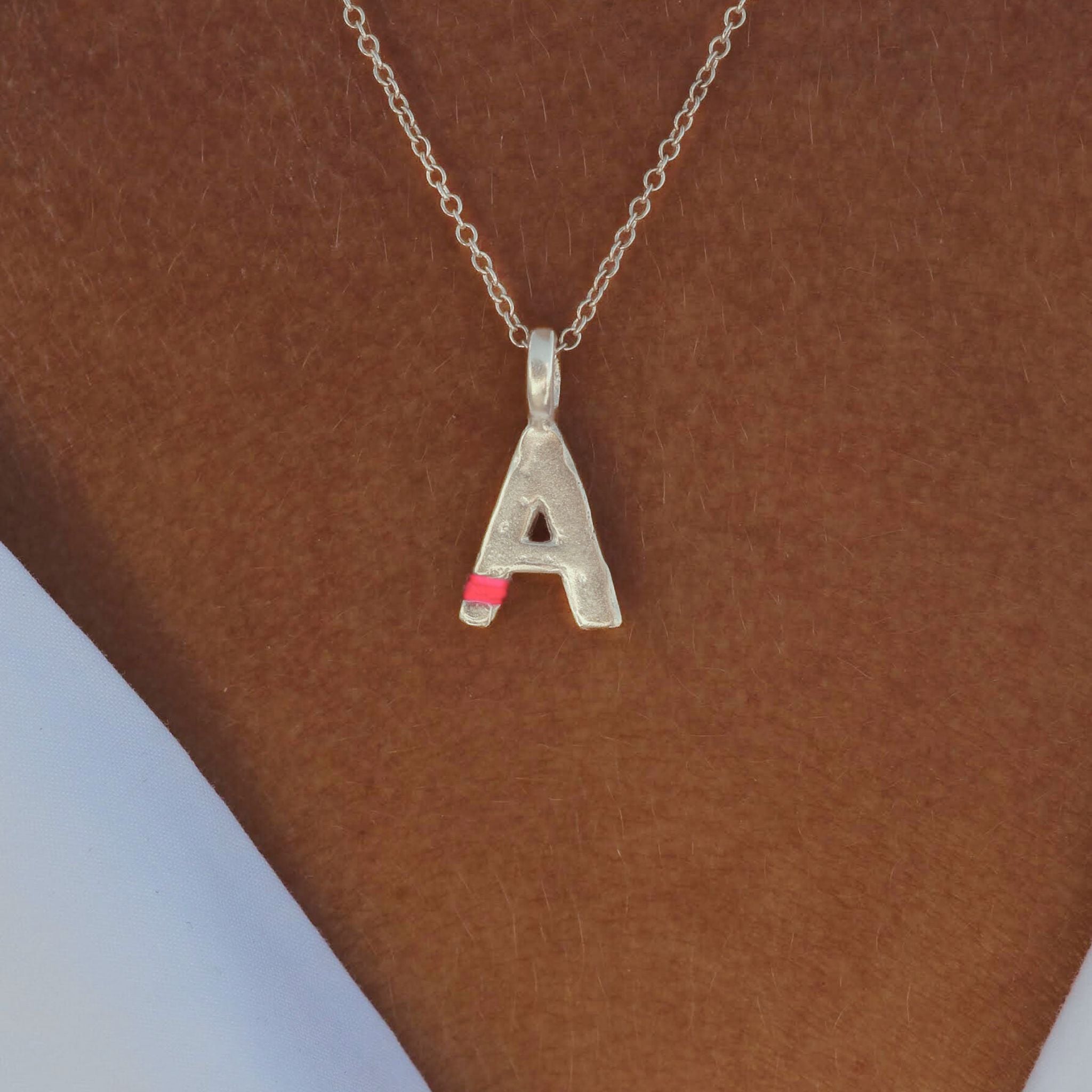 Silver necklace with a letter 'A' pendant on a brown background