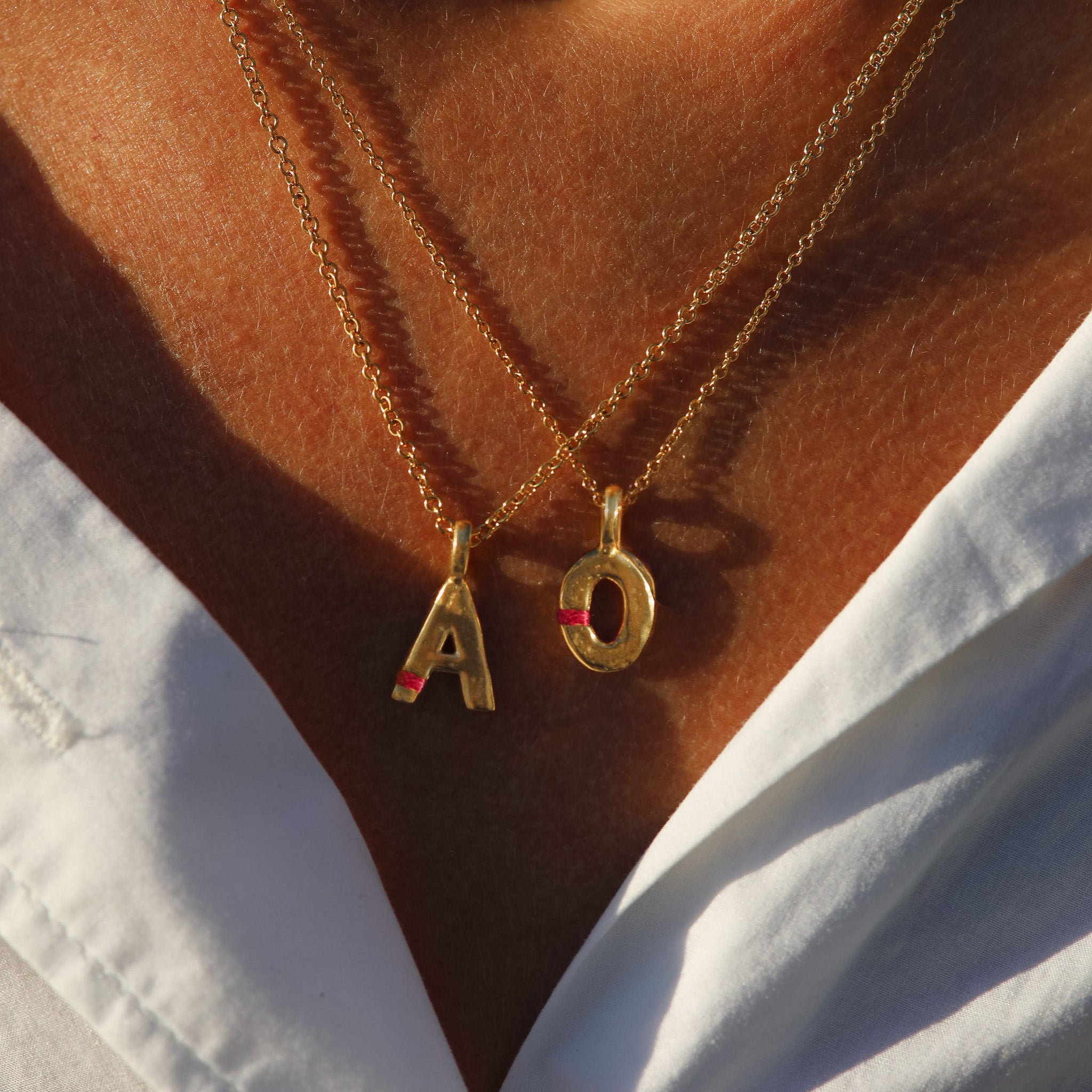 Gold necklaces with 'A' and 'O' pendants on a person wearing a white shirt.