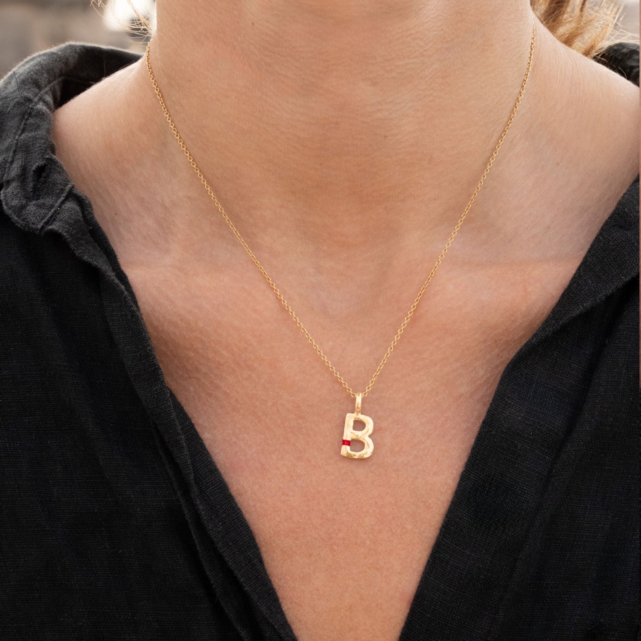 Gold necklace with a 'B' pendant worn by a person in a black outfit.