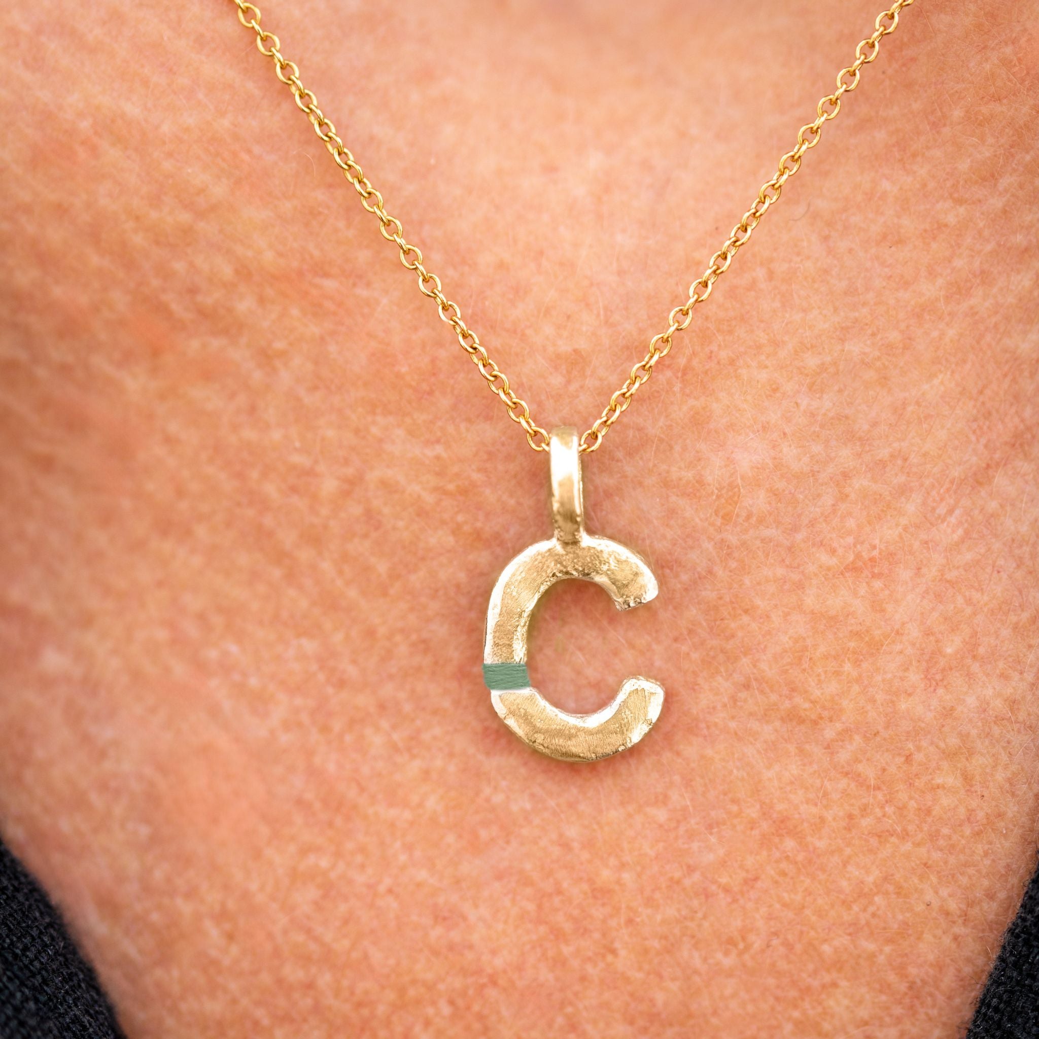 Gold necklace with a 'C' pendant on a person's neck