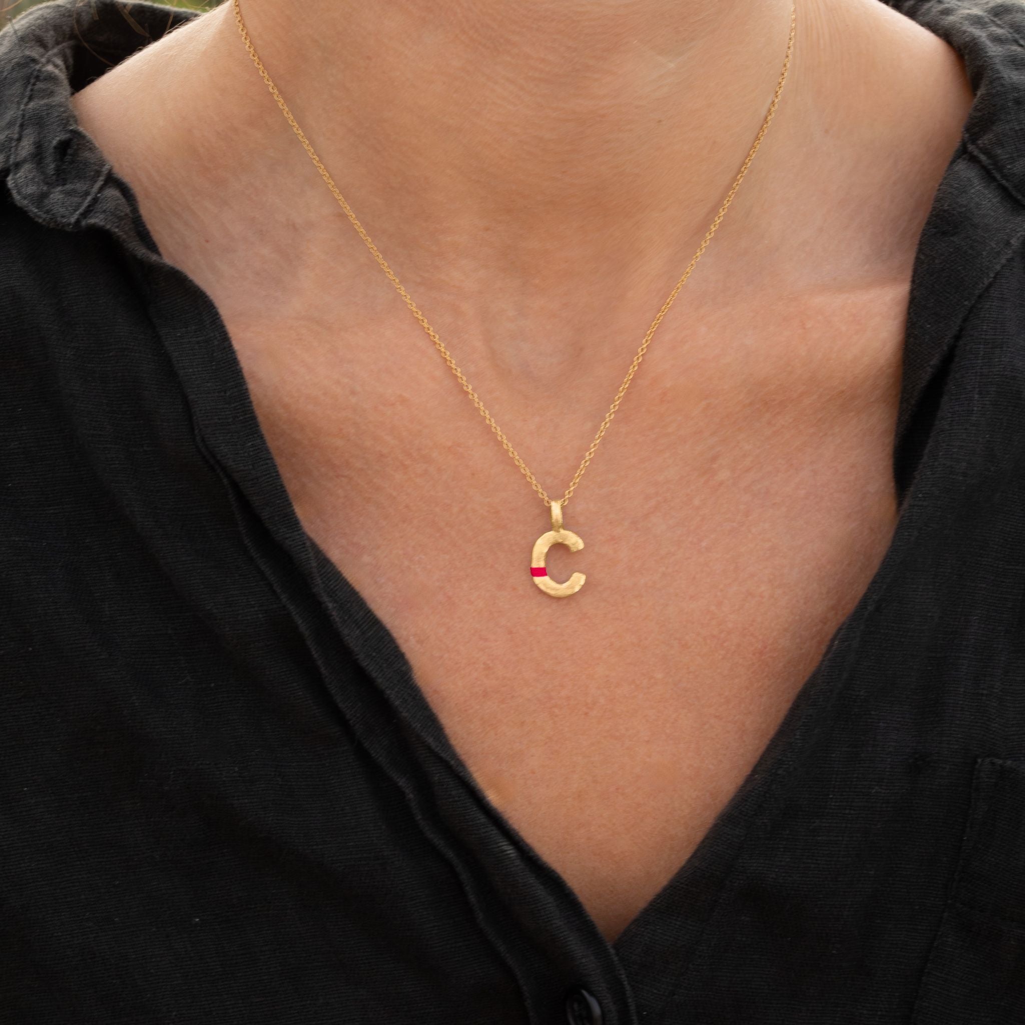 Gold necklace with a 'C' pendant on a person wearing a black garment.