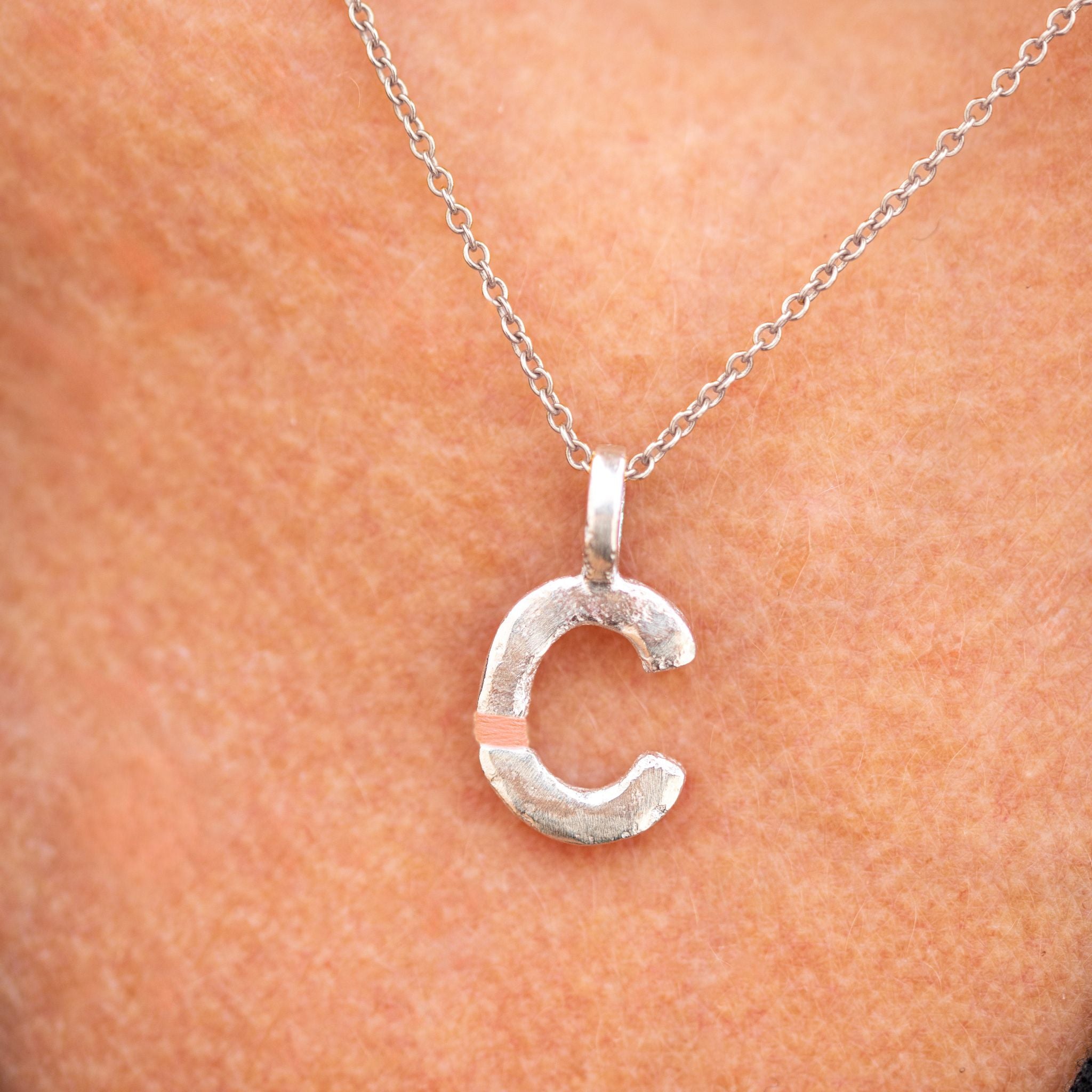 Silver necklace with a 'C' pendant on a person's neck