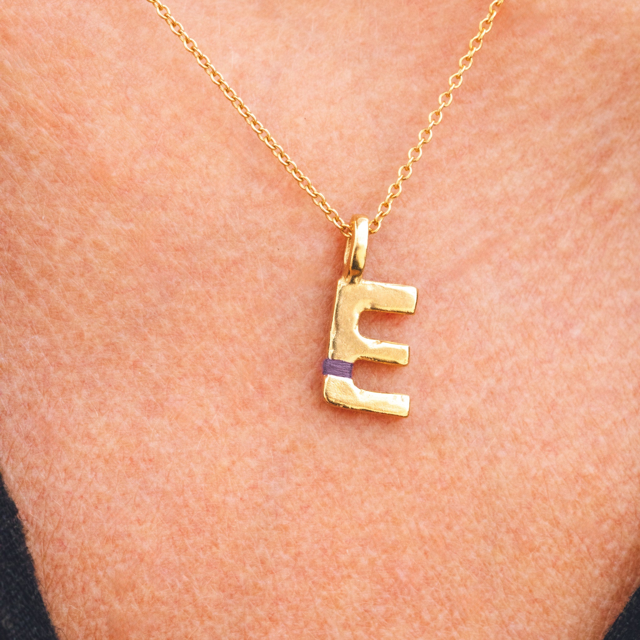Gold necklace with a 'E' pendant on a person's neck