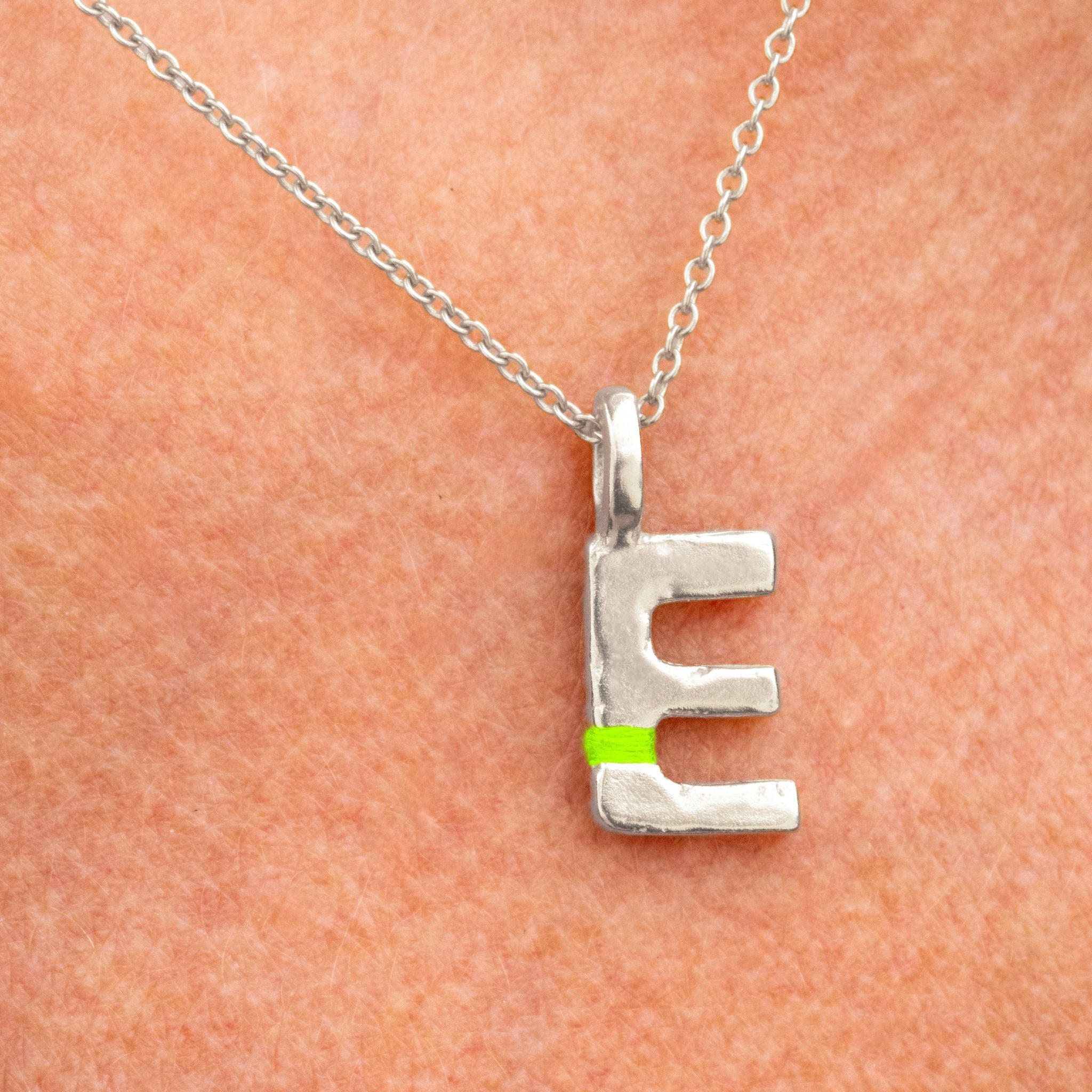 Silver necklace with a letter 'E' pendant on a peach-colored background