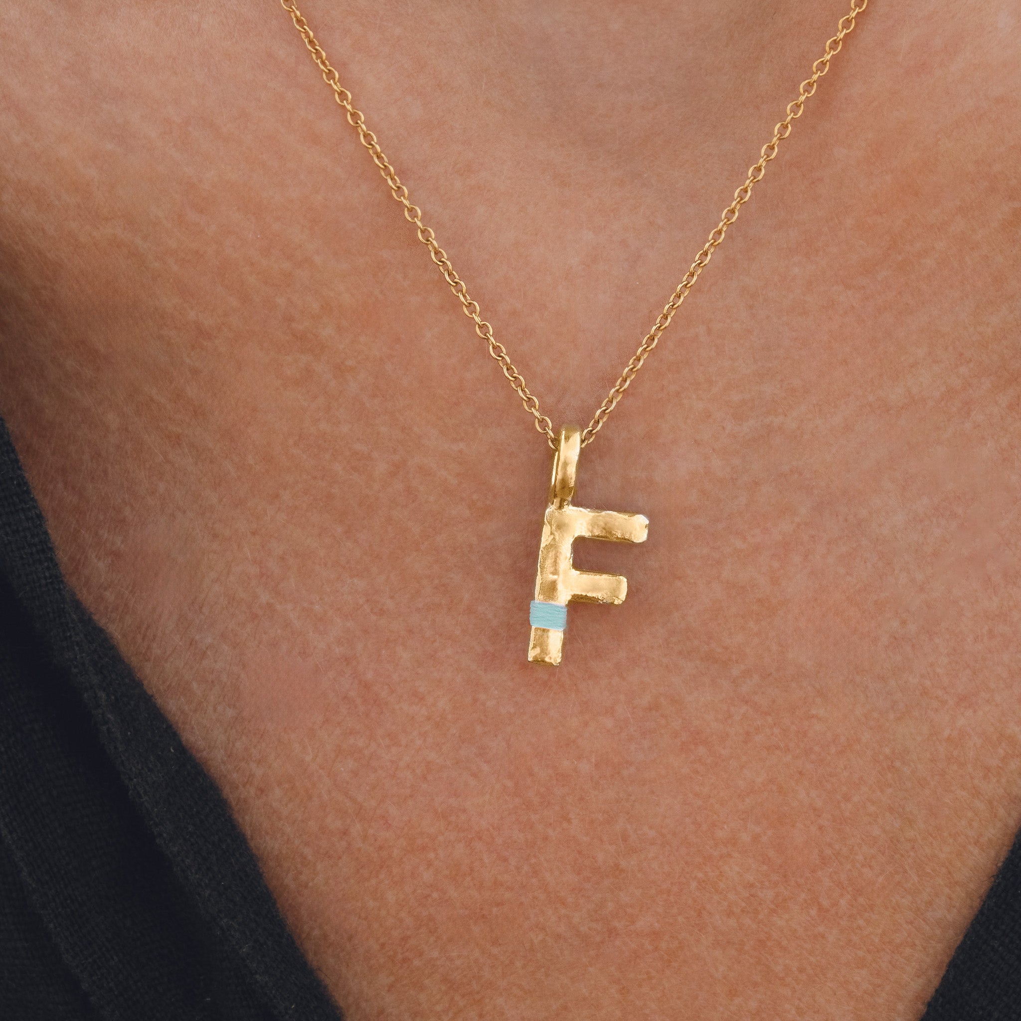 Gold necklace with a 'F' pendant on a person's neck