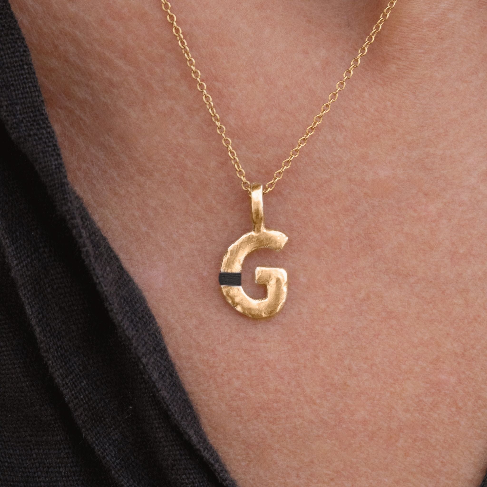 Gold necklace with a letter 'G' pendant on a person's neck.