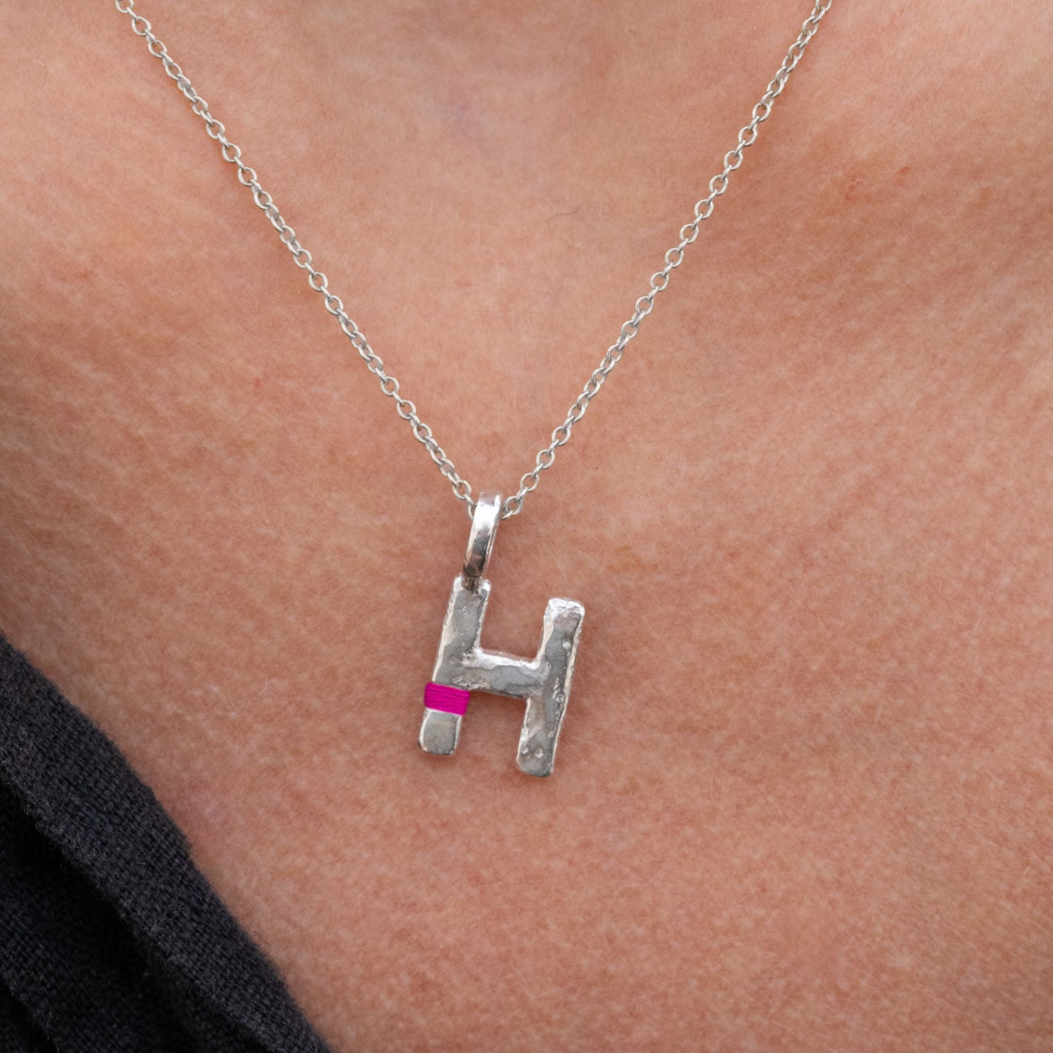 Silver necklace with a letter 'H' pendant on a person's neck