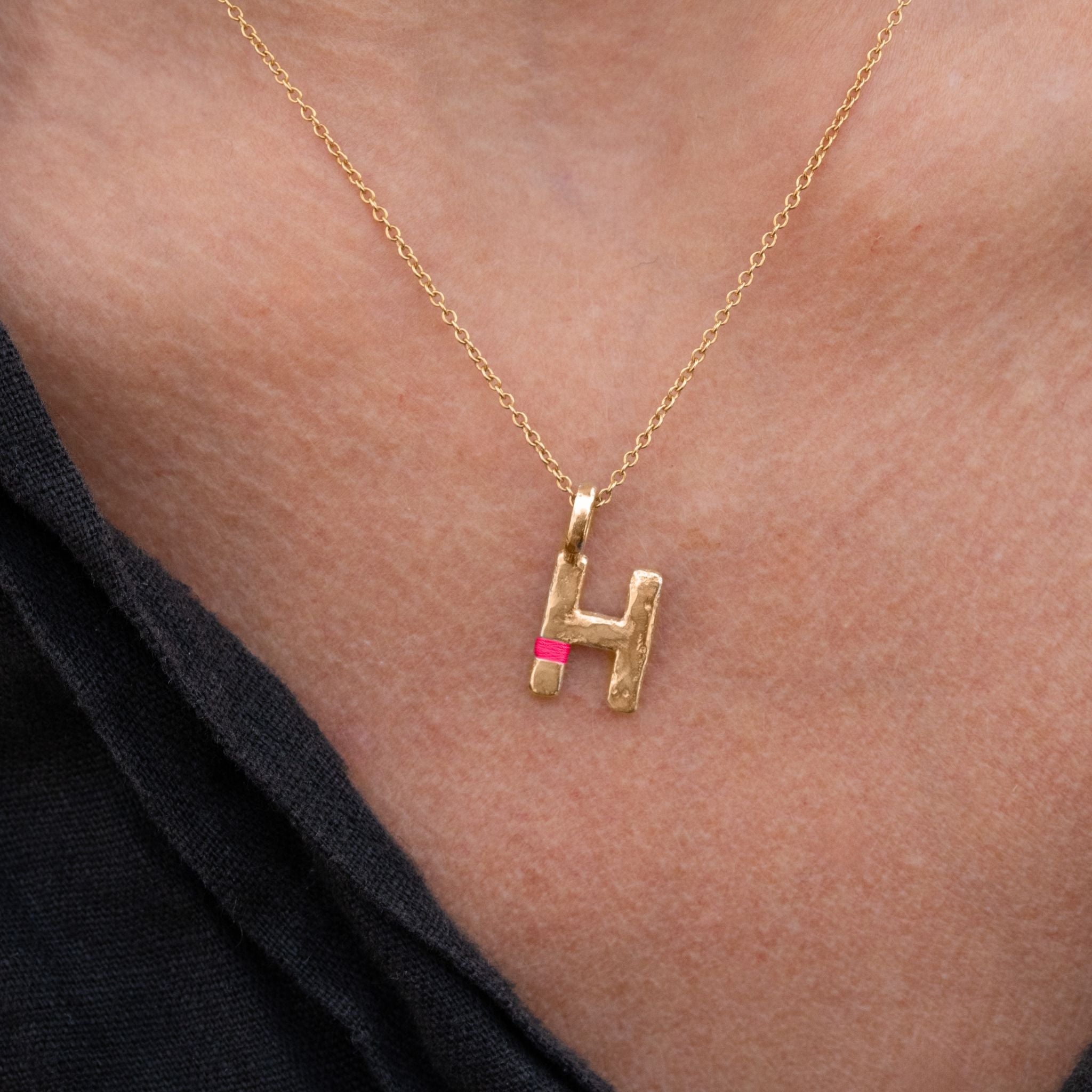Gold necklace with a 'H' pendant on a person's neck