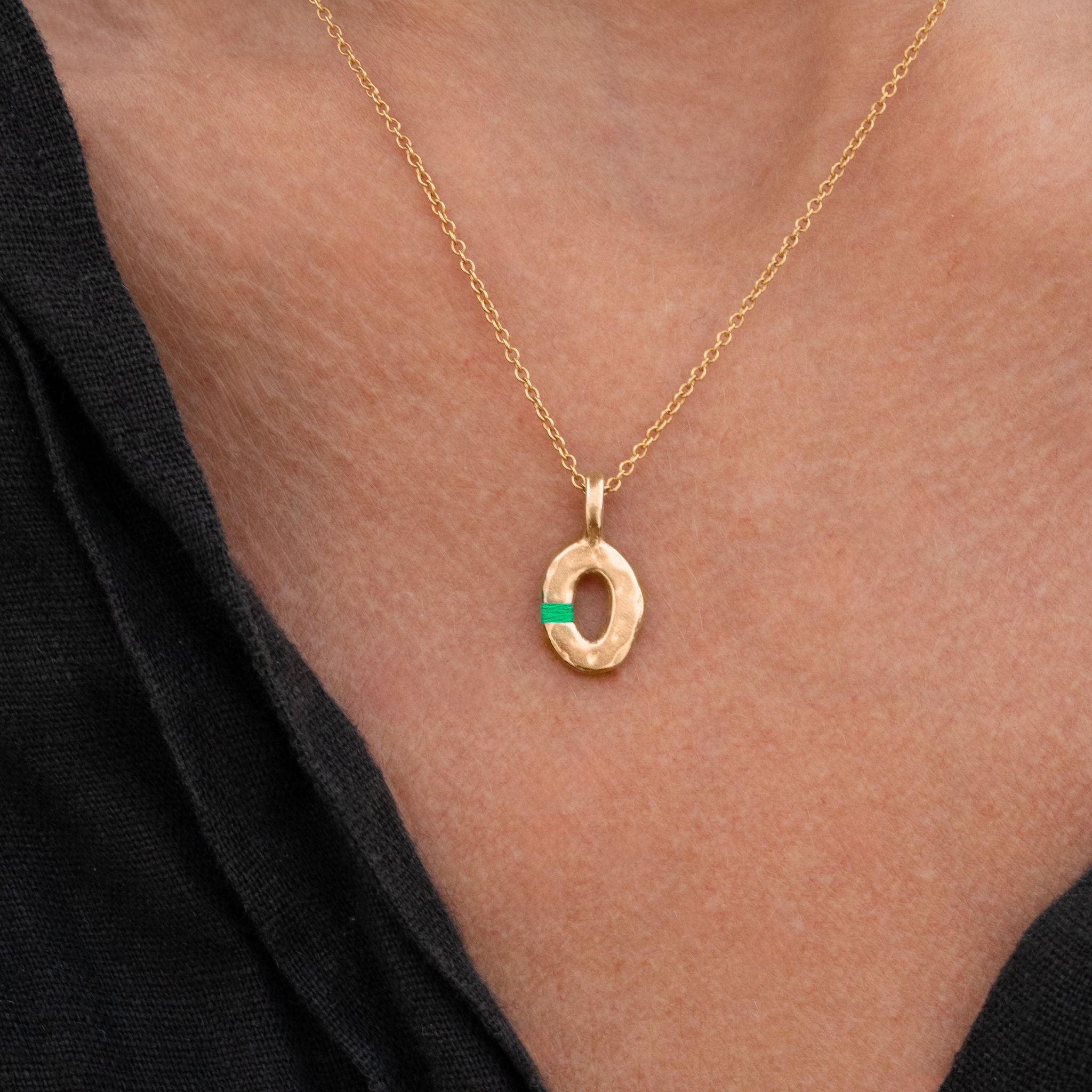 Gold necklace with a green gemstone pendant on a person wearing a black top.
