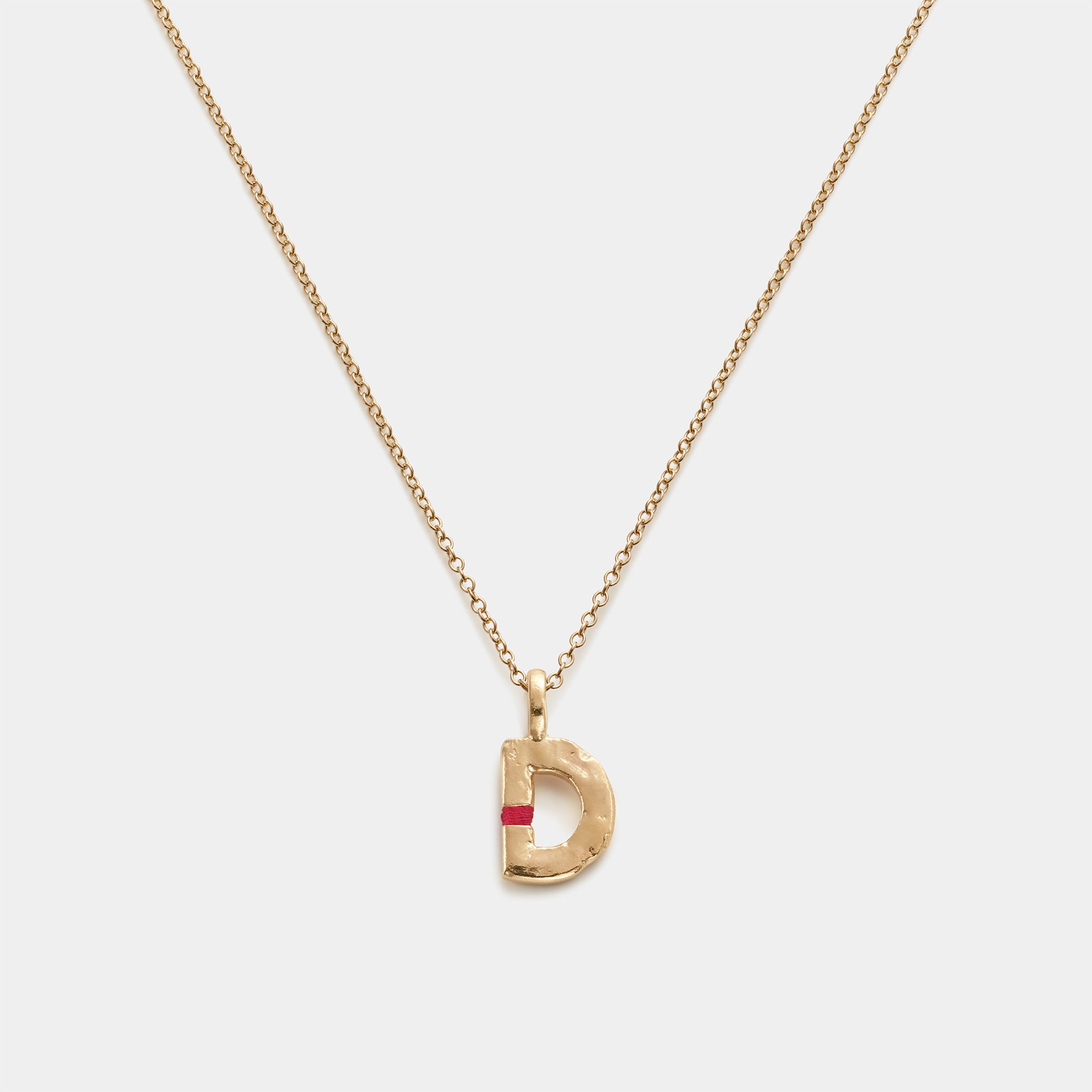 Gold necklace with a 'D' pendant on a light gray background